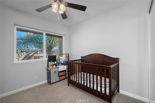 carpeted bedroom featuring a nursery area and ceiling fan