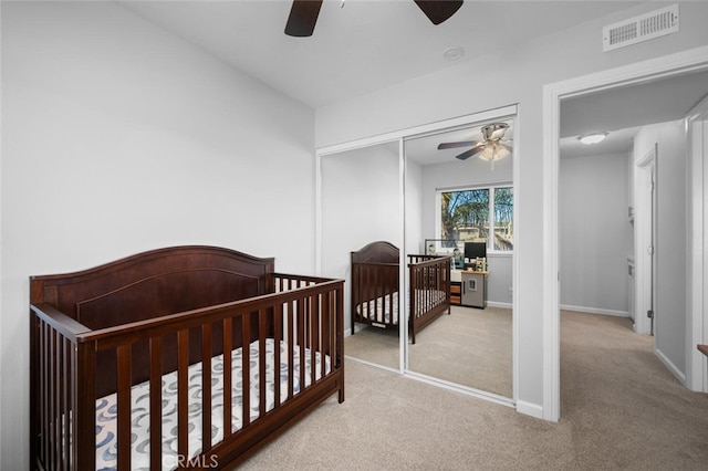 carpeted bedroom featuring a crib, ceiling fan, and a closet