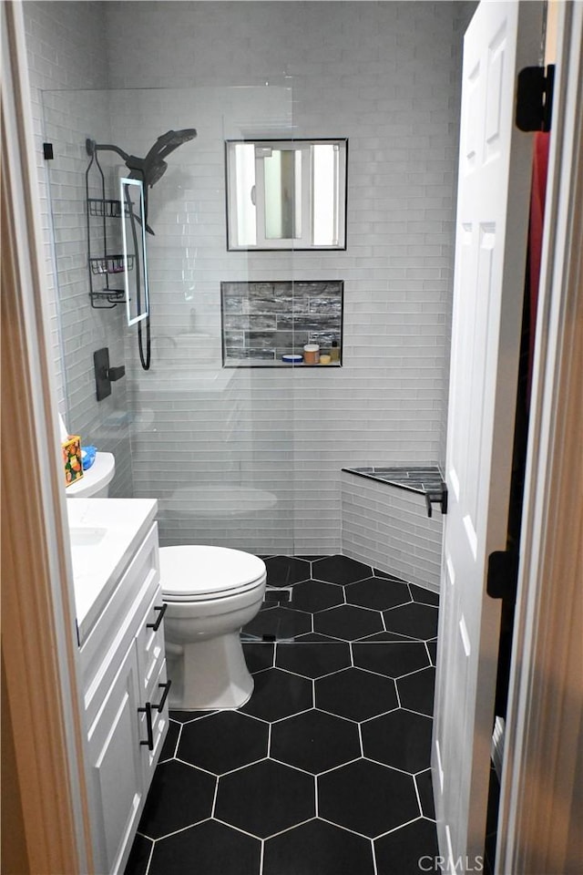 bathroom featuring vanity, tile patterned floors, toilet, and a tile shower