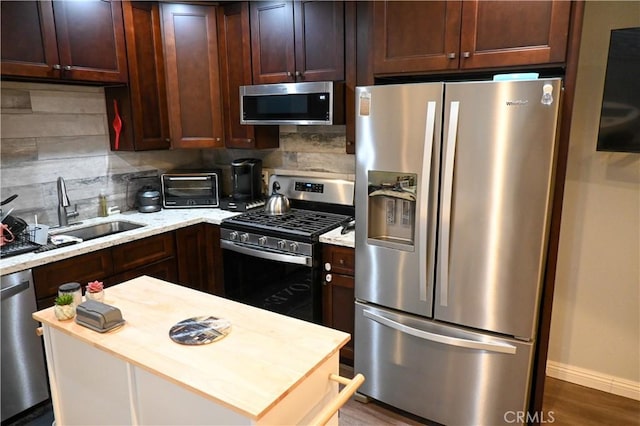 kitchen featuring sink, backsplash, stainless steel appliances, light stone counters, and dark hardwood / wood-style flooring