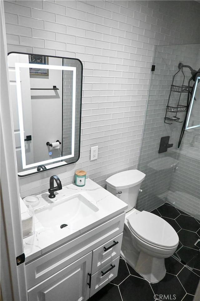 bathroom with tile patterned flooring, tile walls, tiled shower, vanity, and toilet