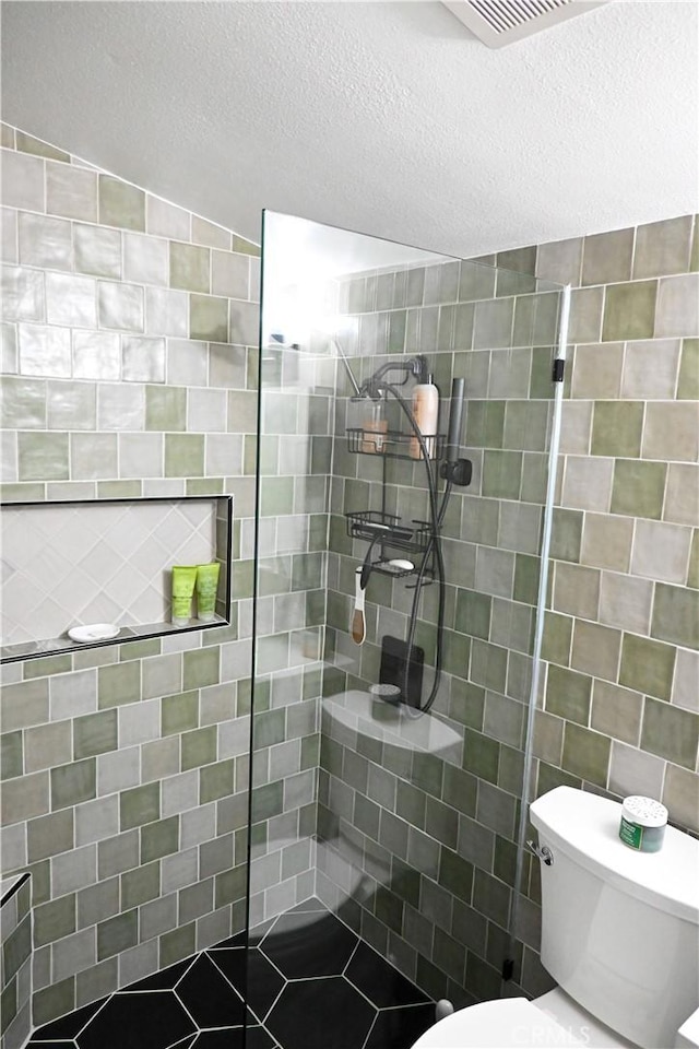 bathroom featuring toilet, tile walls, a textured ceiling, and a tile shower