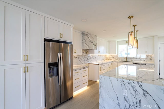 kitchen with stainless steel refrigerator with ice dispenser, white cabinetry, sink, hanging light fixtures, and light stone counters