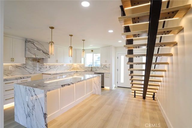 kitchen with stainless steel dishwasher, white cabinetry, a center island, and light stone counters