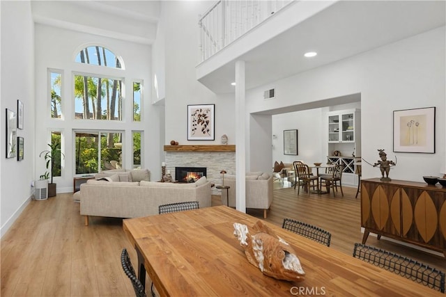 dining space featuring a towering ceiling, a stone fireplace, and light wood-type flooring