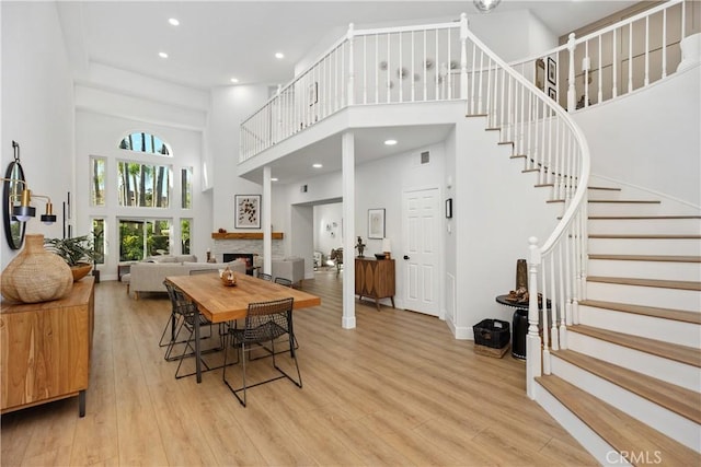 dining area with a towering ceiling, light hardwood / wood-style flooring, and a stone fireplace