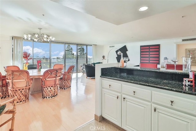 kitchen with a notable chandelier, white cabinets, decorative light fixtures, dark stone countertops, and light hardwood / wood-style flooring