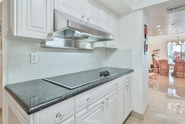 kitchen featuring white cabinetry, black electric stovetop, dark stone countertops, decorative backsplash, and a notable chandelier