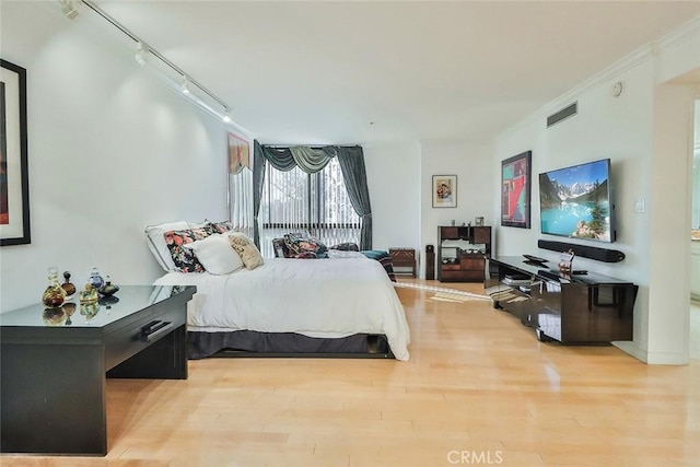 bedroom featuring rail lighting, wood-type flooring, and crown molding