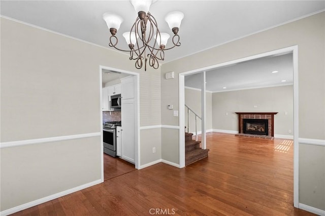 unfurnished dining area with crown molding, a brick fireplace, hardwood / wood-style floors, and a notable chandelier