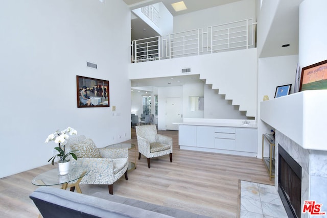 living room with light hardwood / wood-style floors, a tiled fireplace, and a towering ceiling