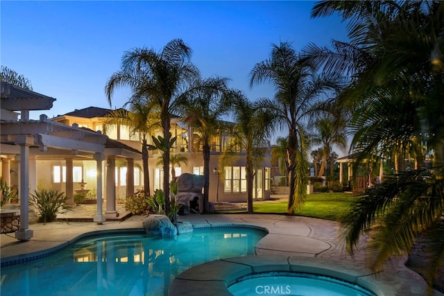 pool at dusk with an in ground hot tub, a lawn, a patio area, and a pergola