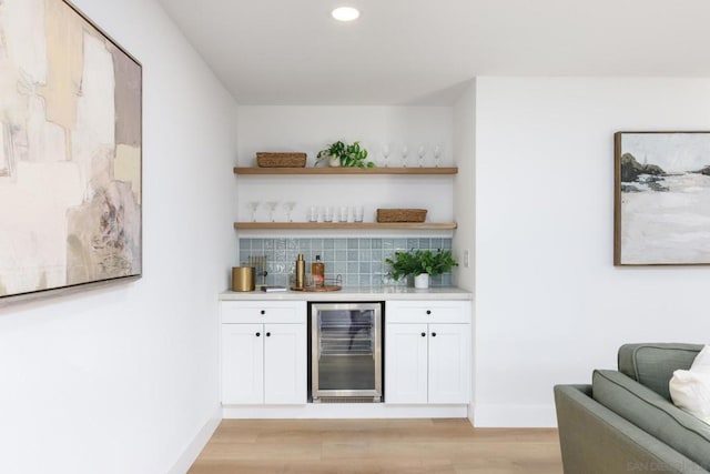 bar featuring light wood-type flooring, white cabinetry, decorative backsplash, and beverage cooler