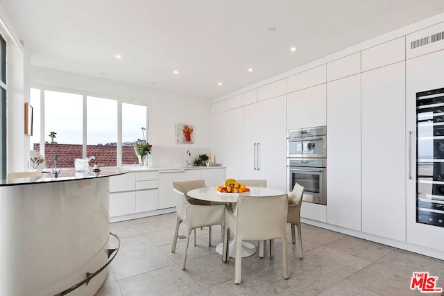 kitchen featuring double oven, sink, white cabinetry, a kitchen bar, and a center island