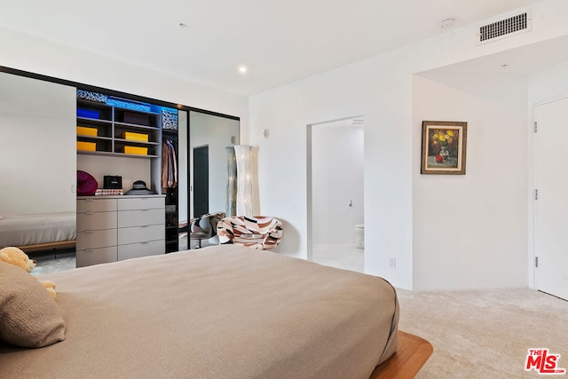 bedroom featuring a closet, light colored carpet, and ensuite bath