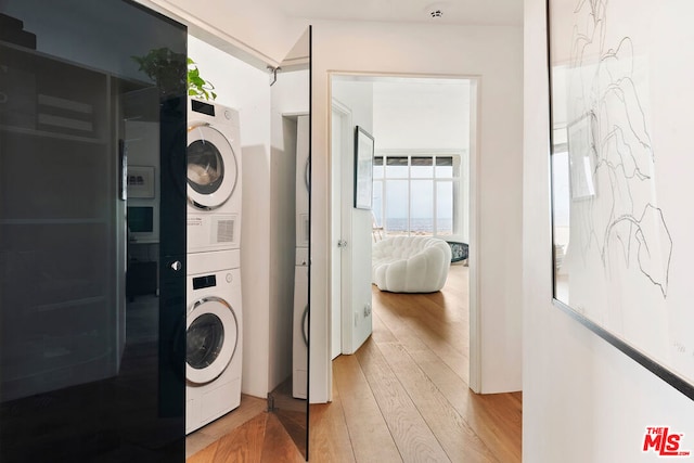 laundry area with stacked washer / drying machine and light wood-type flooring