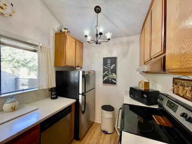 kitchen featuring pendant lighting, appliances with stainless steel finishes, a textured ceiling, light hardwood / wood-style floors, and a chandelier