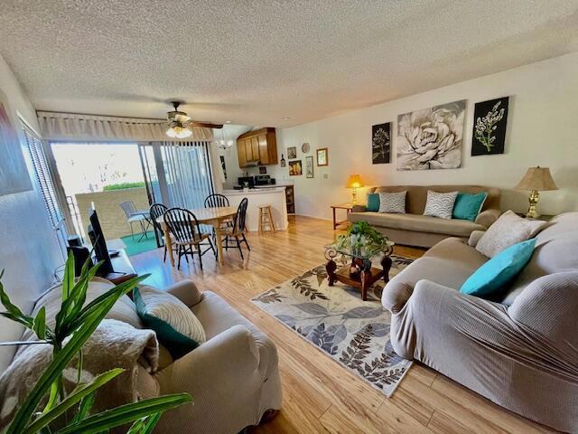 living room with light hardwood / wood-style floors, a textured ceiling, and ceiling fan