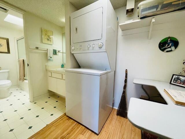 washroom featuring light hardwood / wood-style floors, stacked washer / dryer, and a textured ceiling