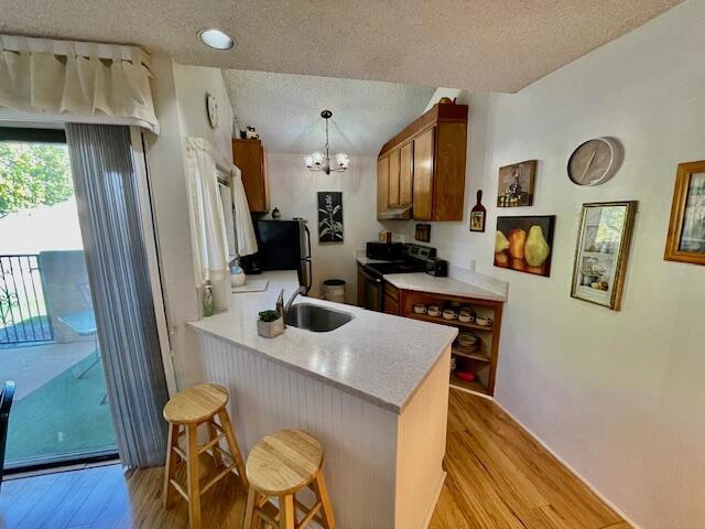 kitchen with a textured ceiling, black electric range oven, a kitchen breakfast bar, light hardwood / wood-style flooring, and kitchen peninsula