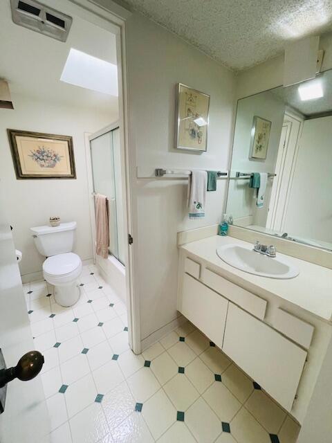 full bathroom with vanity, shower / bath combination with glass door, a textured ceiling, and toilet