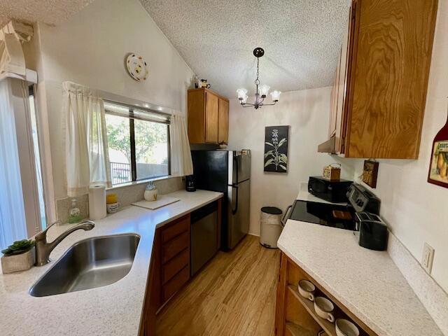 kitchen featuring appliances with stainless steel finishes, a textured ceiling, sink, light wood-type flooring, and pendant lighting