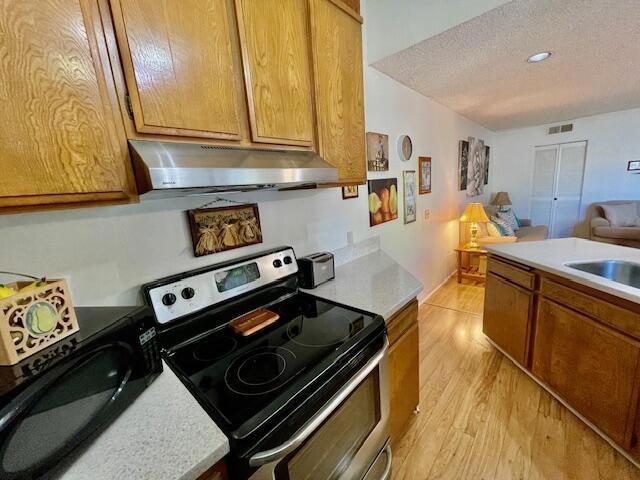 kitchen with sink, stainless steel electric stove, light hardwood / wood-style floors, and a textured ceiling