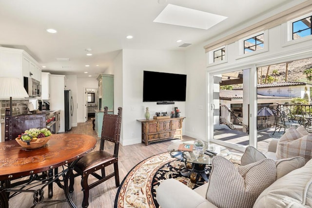 living room with light hardwood / wood-style floors, a wealth of natural light, and a skylight