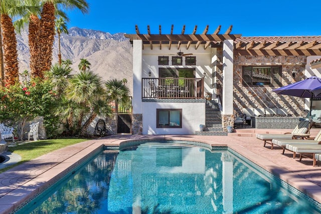 rear view of house featuring a pergola, exterior fireplace, a mountain view, a balcony, and a patio area