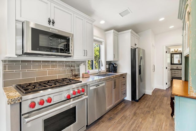 kitchen with light stone countertops, white cabinets, dark hardwood / wood-style flooring, stainless steel appliances, and sink