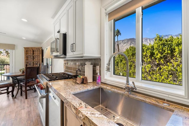 kitchen with appliances with stainless steel finishes, sink, a mountain view, decorative backsplash, and lofted ceiling