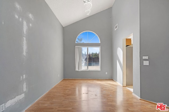 unfurnished living room featuring high vaulted ceiling, light hardwood / wood-style floors, and a textured ceiling