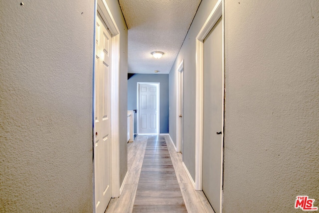 hall featuring light hardwood / wood-style floors and a textured ceiling