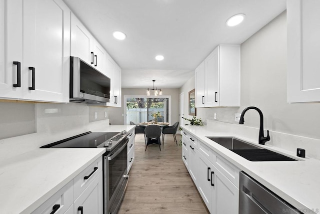 kitchen with pendant lighting, appliances with stainless steel finishes, sink, light wood-type flooring, and white cabinetry