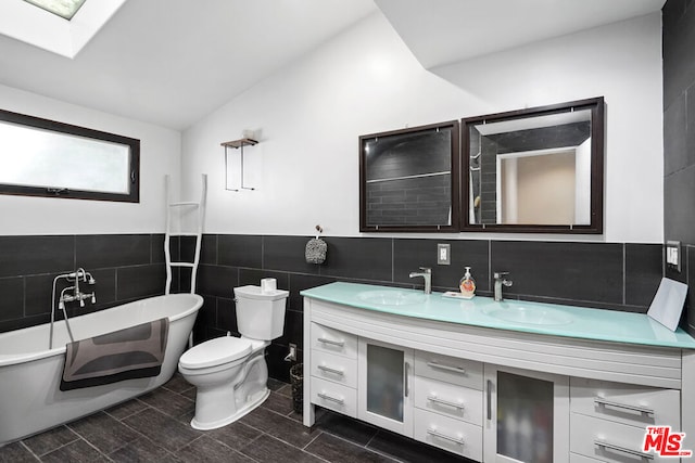 bathroom with vanity, tile walls, toilet, vaulted ceiling, and a washtub