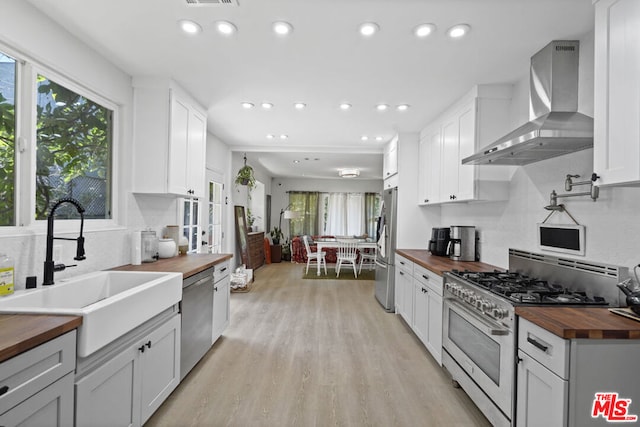 kitchen featuring white cabinets, sink, wood counters, stainless steel appliances, and wall chimney exhaust hood