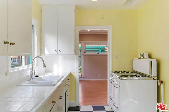 kitchen with sink, white cabinets, gas range gas stove, and tile counters