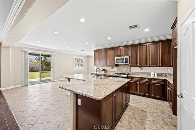 kitchen featuring sink, ornamental molding, an island with sink, and light stone countertops