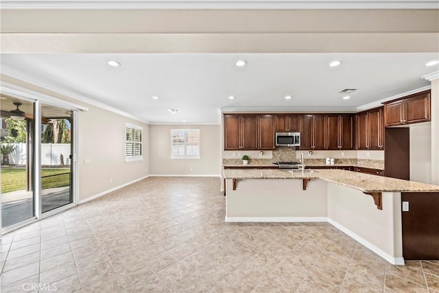 kitchen with sink, a breakfast bar area, ornamental molding, an island with sink, and light stone countertops