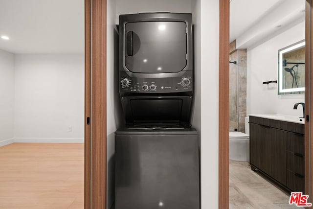 laundry area featuring sink, stacked washer and dryer, and light wood-type flooring