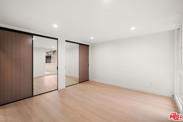 unfurnished bedroom featuring two closets and light wood-type flooring