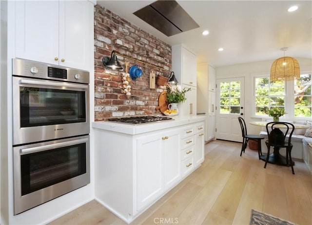 kitchen featuring light hardwood / wood-style floors, white cabinets, pendant lighting, and appliances with stainless steel finishes