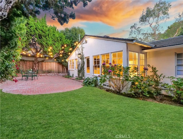 back house at dusk featuring a lawn and a patio