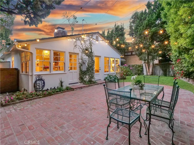 back house at dusk with a patio area and a lawn