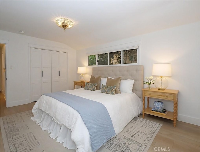 bedroom featuring a closet, light wood-type flooring, and vaulted ceiling