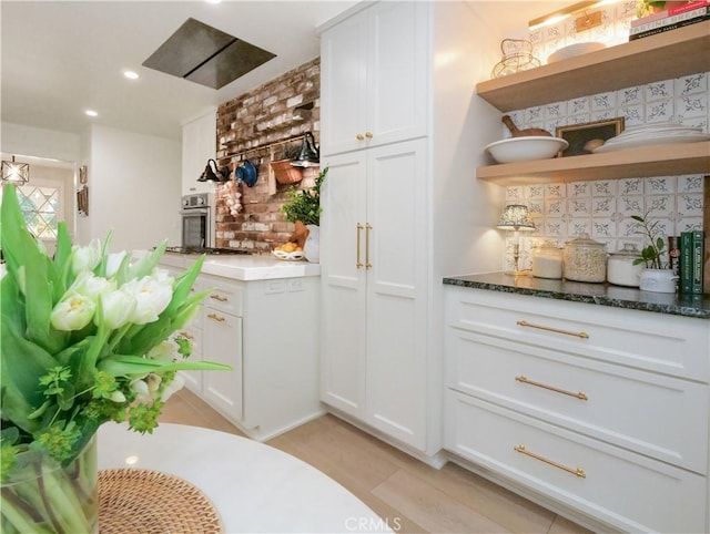 bar featuring decorative backsplash, white cabinetry, dark stone counters, and stainless steel oven