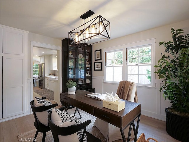 home office with light hardwood / wood-style floors and a notable chandelier