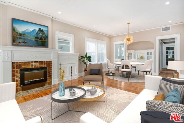 living room featuring a notable chandelier, crown molding, a tiled fireplace, and light wood-type flooring