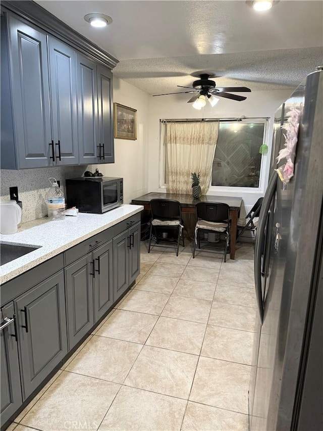 kitchen with ceiling fan, appliances with stainless steel finishes, a textured ceiling, and light tile patterned flooring