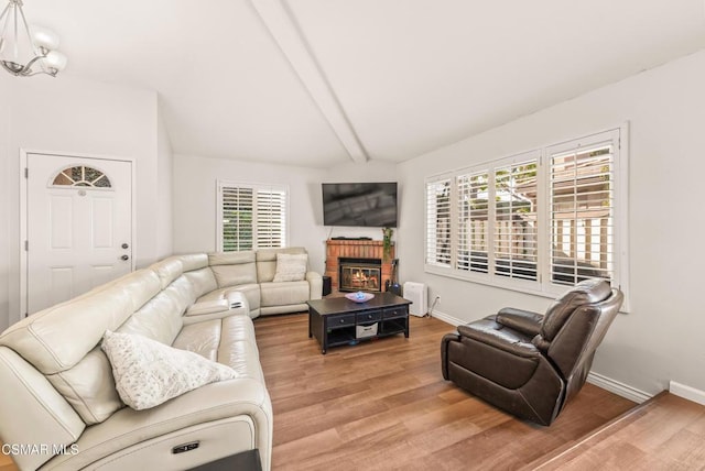 living room featuring hardwood / wood-style flooring, vaulted ceiling with beams, a chandelier, and a fireplace